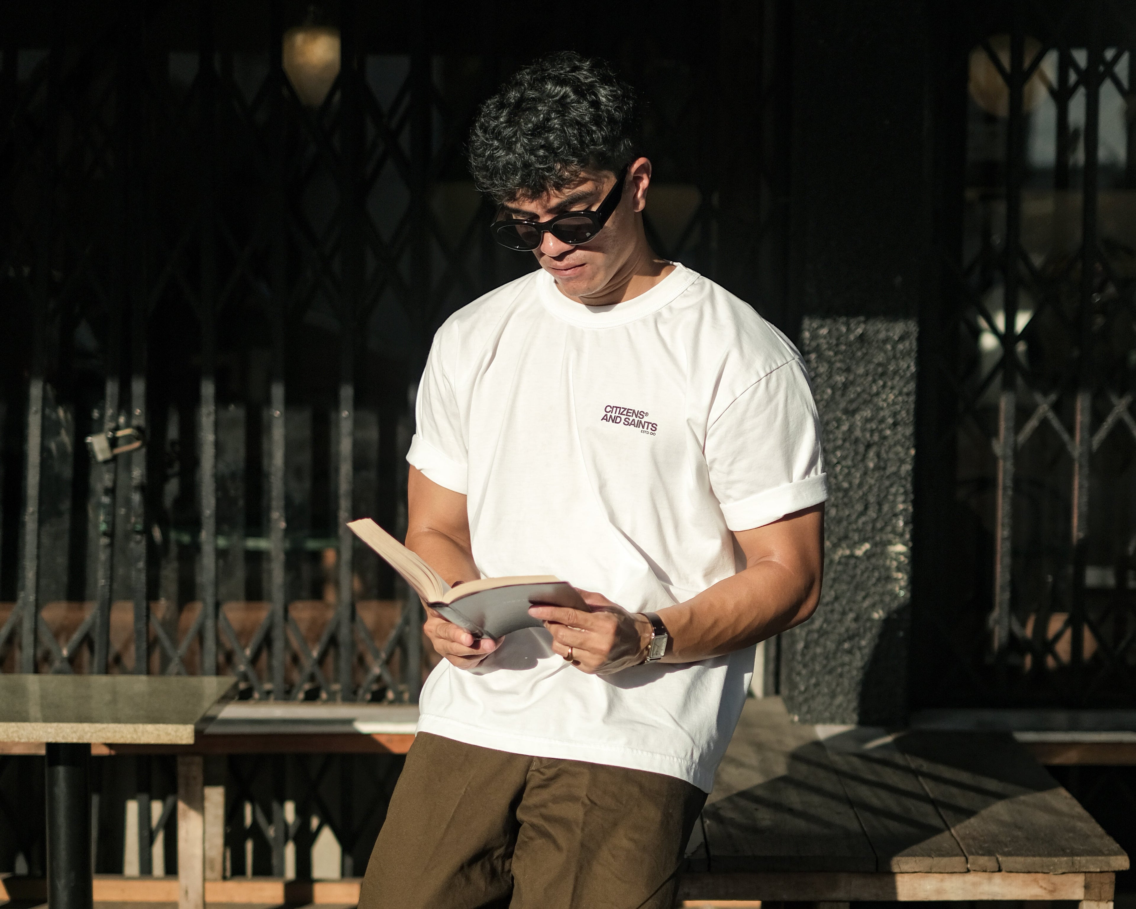 Man sitting on a bench reading a book in an outdoor setting